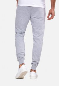 Graue Baumwoll-Jogginghosen mit tapered Bein-Design, gerippten Bündchen und weicher Textur, kombiniert mit weißen Turnschuhen.