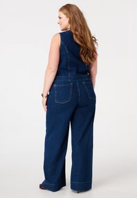 Denim jumpsuit met een slim fit mouwloos bovenstuk en wijde broekspijpen. Donkerblauwe kleur met zichtbare stiksels en twee achterzakken.