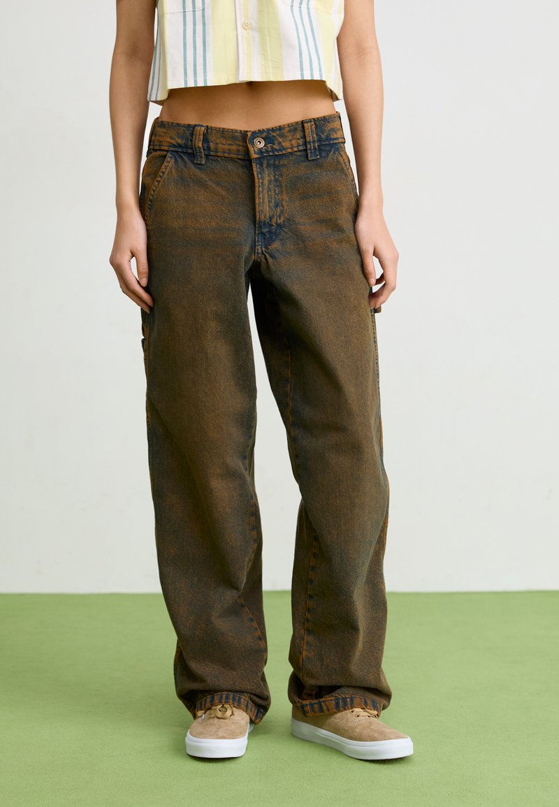 Pantaloni larghi in denim scuro con una trama sbiadita, dotati di chiusura a bottone, cinque tasche e cuciture decorative. Indossati con un top a righe corto.