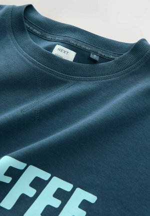 Sweatshirt bleu marine avec un col rond, un col côtelé et un texte bleu clair "COFFEE". Présente une texture de tissu lisse et des détails de couture visibles.
