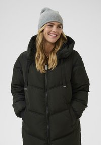 Sort puffjakke med hætte, der har stikninger og en frontlynlås. Bæres med en lysegrå strikket hue. Glat tekstur.