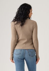 Top de manga larga beige con diseño acanalado y silueta ajustada, combinado con jeans de color azul claro que tienen bolsillos traseros y un estilo clásico.