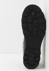 Semelle en caoutchouc noir avec un motif de semelle texturé, dotée d'un dessus en cuir gris. Logo estampé près du talon avec la taille 42 visible.