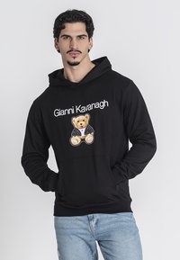 Sudadera negra con capucha que presenta un gráfico de un oso de peluche y el texto "Gianni Kavanagh". Tela suave, corte relajado y puños acanalados.