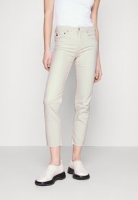 Beige slim fit džíny s vysokým pasem a zkrácenou délkou. Mají přední kapsy, zip a béžovou elastickou tkaninu. Boty s černou podrážkou.