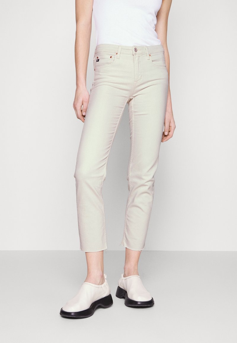 Beige slim fit džíny s vysokým pasem a zkrácenou délkou. Mají přední kapsy, zip a béžovou elastickou tkaninu. Boty s černou podrážkou.