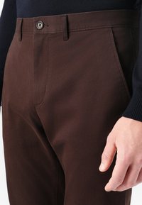 Barna pamut nadrág sima textúrával, gombos záródással, övhurkokkal és oldalsó zsebekkel. Az anyag finom fényességgel rendelkezik.