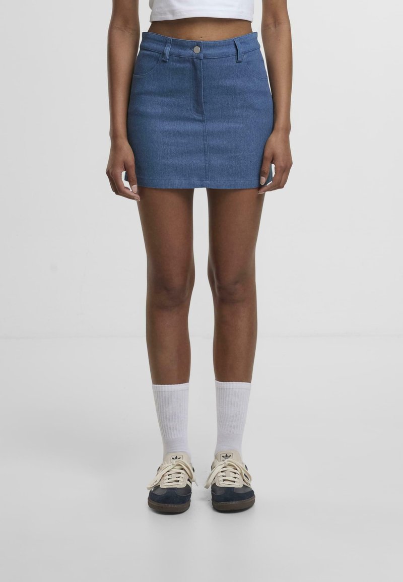 Sinili denim mini skirta, na may fitted na disenyo, harapang pindutan na pagsasara, at dalawang side pockets. Kasama ng puting medyas at madidilim na sneakers.