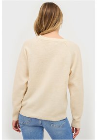 Beige trui met een zachte textuur, geribbelde mouwen en zoom, en raglan mouwen, gecombineerd met denim jeans.