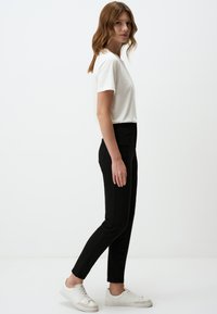 Czarne dżinsy w połączeniu z białą koszulką z krótkim rękawem. Obuwie to białe trampki. Styl jest prosty, o klasycznym kroju, bez dodatkowych zdobień.