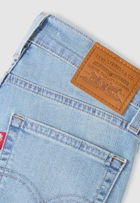 Ανοιχτό μπλε τζιν παντελόνι με πίσω τσέπη, καφέ δερμάτινο ταμπελάκι με το λογότυπο Levi's και μικρή κόκκινη υφασμάτινη ετικέτα Levi's στη ραφή πλευράς.