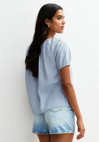 Gestreepte blouse in lichtblauw en wit, met korte poffende mouwen en een geplooide achterkant, gecombineerd met lichtblauwe denimshorts.
