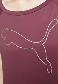Burgundy träningsskjorta med en slät yta, med en vit kontur av en hoppande pumalogo över framsidan. Rund halsringning.