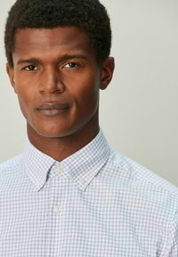 Nappisuljettava paita valkoisella ja vaaleansinisellä ruutukuvioinnilla, jossa on leveä kaulus ja kaksi nappisuljetusta, valmistettu sileästä kankaasta.