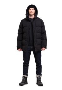 Chaqueta acolchada negra con capucha, cremallera frontal y bolsillos, combinada con jeans de denim oscuro y botas impermeables negras.