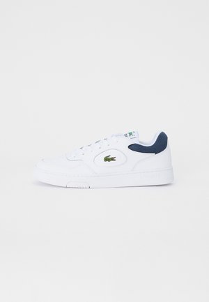 Białe niskie sneakersy z granatowymi akcentami, skórzane o teksturowanej powierzchni, okrągły czubek, wzór sznurowania oraz wyhaftowane zielone logo krokodyla po boku.