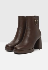 Bruine leren enkellaarsjes met een chunky vierkante hak, met een zijnaaddetail en een kettingaccent aan de achterkant. Glide textuur.
