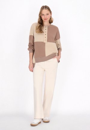 Felpa beige e marrone stampata a blocchi con scollo a V bottonato e polsini a costine, abbinata a pantaloni larghi crema e sneakers bianche.