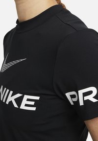 Černé sportovní tričko z hladké látky s bílým logem Nike na hrudi a bílým nápisem "PRO" na rukávu. Vysoký výstřih.