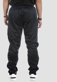 Schwarze Trainingshose mit elastischem Bund, glatter, glänzender Textur, taillierter Beinform und gerafften Bündchen. Getragen mit weißen Sneakers.