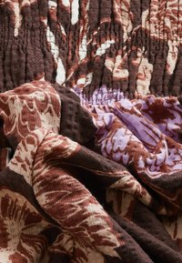 Bunt gemusterter Stoff mit glatter Textur, der braune, cremefarbene und lavendelfarbene Blumenmuster zeigt; gerafftes und plissiertes Designdetail.