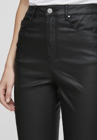 Musthave musta имitatsioon nahast kõrgema vöökohtadega püksid, millel on tekstuuriga viimistlus, esifrotee ja hõbedane riistvara nööbi ja nupudena.