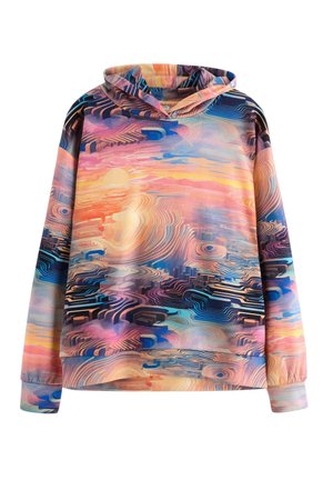 Teenagedreng iført hættetrøje med flerfarvet abstrakt mønster, cremefarvede bukser og hvide sneakers, gående mod en ensfarvet lys baggrund.