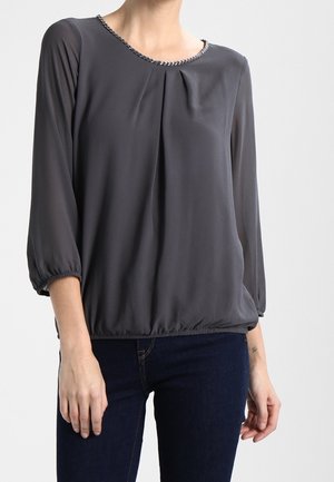 Blusa grigia con maniche a tre quarti, davanti plissettato e scollatura arrotondata decorata con un bordo decorativo. Tessuto morbido e leggero.