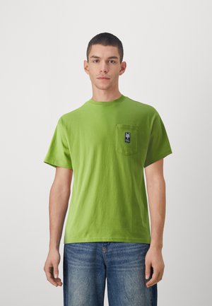 Grønn bomulls T-skjorte med korte ermer, rund hals og en brystlomme med en mørk blå etikett. Båret med blå jeans.