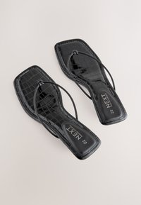 Paar schwarze croc-geprägte Sandalen mit quadratischer Spitze, dünnen Riemen und gebrandeten Innensohlen auf hellem Hintergrund.