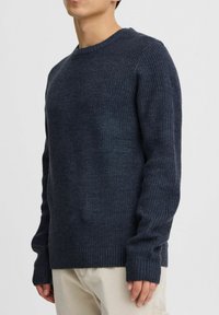 Navy ribbed knit sweater with a crew neckline, long sleeves, and extended cuffs. Made of textured fabric, featuring a relaxed fit.