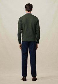Dunkelgrüner Sweatshirt mit langen Ärmeln und Rundhalsausschnitt, kombiniert mit marineblauen Hosen, von hinten betrachtet. Glatte Textur, minimale Details.