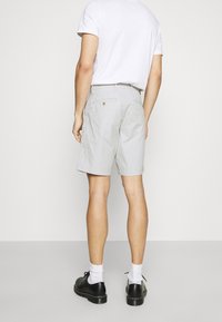 Pantalones cortos de algodón grises con un corte ajustado, que presentan una cinturilla con cierre de botón y bolsillos traseros. Se llevan con una camiseta blanca y zapatos negros.