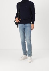Mörkblå polotröja, ljusblå jeans och vita sneakers. Tröjan har en liten logotyp, jeansen har en avslappnad passform och skorna har en slät yta.