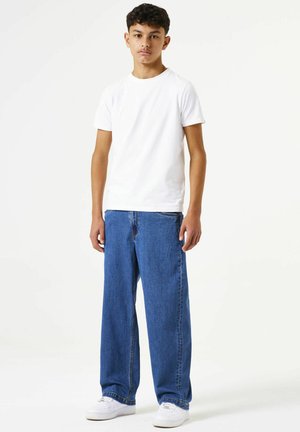 Weißes Baumwoll-T-Shirt kombiniert mit locker sitzender dunkelblauer Denim-Jeans und weißen Sneakers. Einfaches Design, entspannte Silhouette, keine Muster oder Akzente.