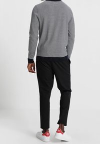 Pullover a righe navy e bianche con scollatura a girocollo, abbinato a pantaloni neri tapered e sneakers bianche con dettagli rossi.