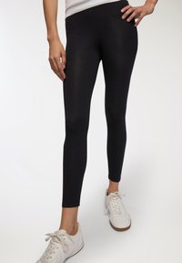 Czarne legginsy wykonane z elastycznego materiału, o dopasowanym kroju i gładkiej fakturze, sięgające do kostek. Zestawione z białymi sneakerami.