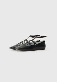 Bailarinas negras con punta afilada y diseño de tiras en T, adornadas con tachuelas circulares a lo largo de la tira. Hechas de cuero suave.