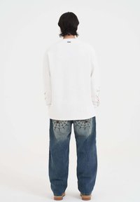 Witte lange mouwen shirt met een ronde hals, gecombineerd met losse blauwe jeans met spinnenweb borduursel op de achterzakken.