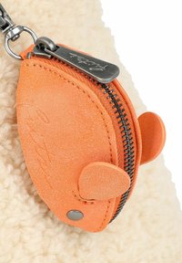 Oranje textuur rondom een ritszakje met een zilveren ritstrekkertje, met ronde oorachtige accenten, geplaatst tegen een pluizige crèmekleurige achtergrond.