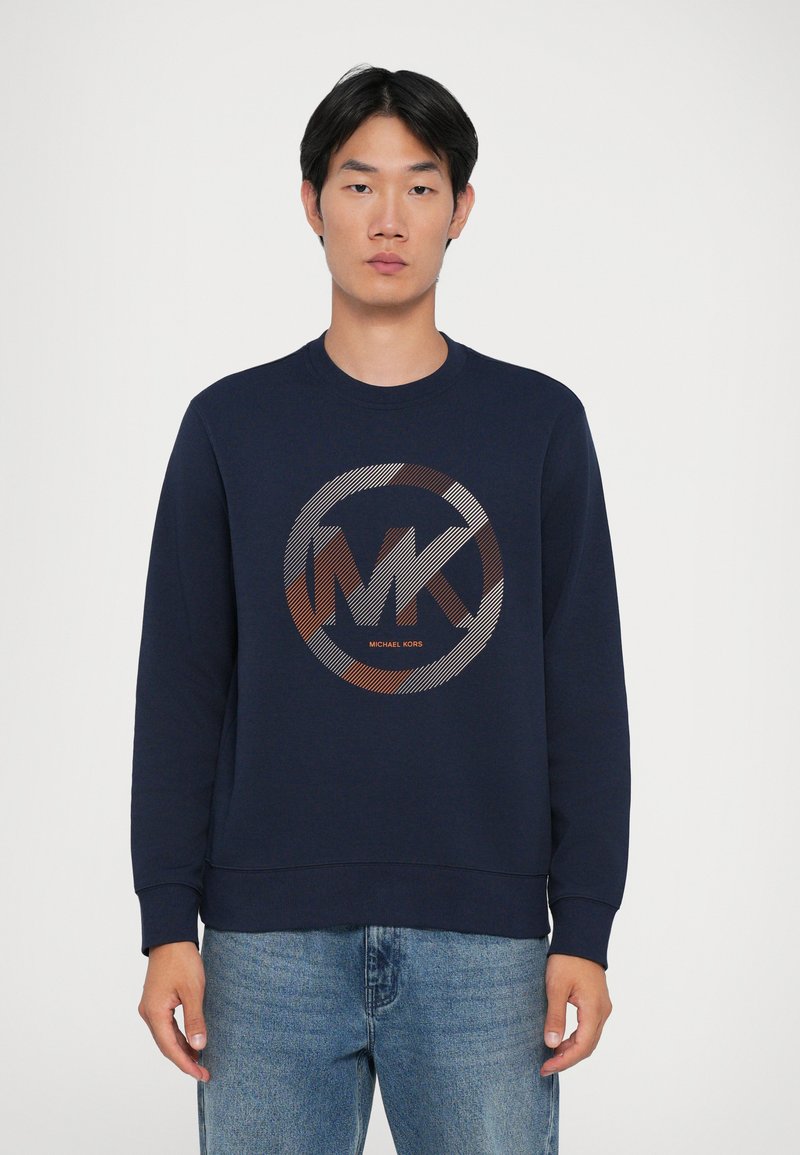 Sweatshirt azul-marinho com um gráfico redondo apresentando o logótipo "MK" em cores metálicas. Gola redonda e punhos canelados, feito de um material têxtil suave.