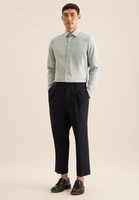 Lichtgroen overhemd met een gestructureerde kraag, gecombineerd met donkerblauwe geplooide broek en zwarte leren schoenen. Glad stoftextuur.