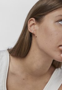 Pendiente de perla única en blanco, de forma redonda. Se lleva en el lóbulo, con una superficie lisa y un diseño minimalista, que resalta el tono de piel.