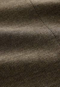 Gros plan d'un tissu tissé marron texturé avec des coutures visibles et des plis doux.