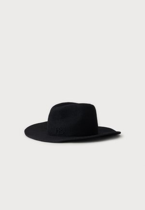 Chapeau fedora noir à large bord en feutre, avec un logo en relief discret sur le côté, présenté sur un fond gris clair.