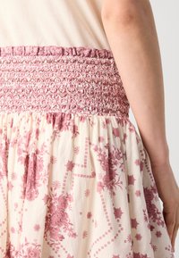 Pink floral-patterned skirt with a shirred waistband, featuring a cream base and subtle decorative details throughout the fabric.