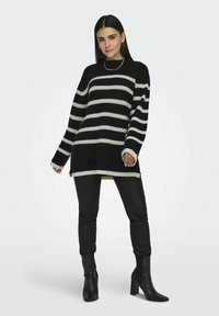 Zwart-wit gestreepte gebreide trui met een losse pasvorm, voorzien van lange mouwen en contrasterende afwerking. Gekleed met zwarte skinny jeans en enkelboots.
