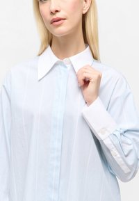 Hellblau gestreiftes Hemd mit einem weißen Kragen und Manschetten, einer einfachen Knopfleiste und einem lässigen Schnitt. Der Stoff wirkt glatt und leicht.