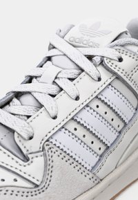 Nærbilde av hvit Adidas-sneakers med tre sydd striper, bundne lisser og Adidas-logo på den polstrede tungen.