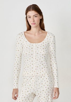 Maglietta a maniche lunghe con scollatura a barca, in tessuto cremoso con stampa floreale nei toni del rosa e del verde, e chiusura frontale con bottoni.